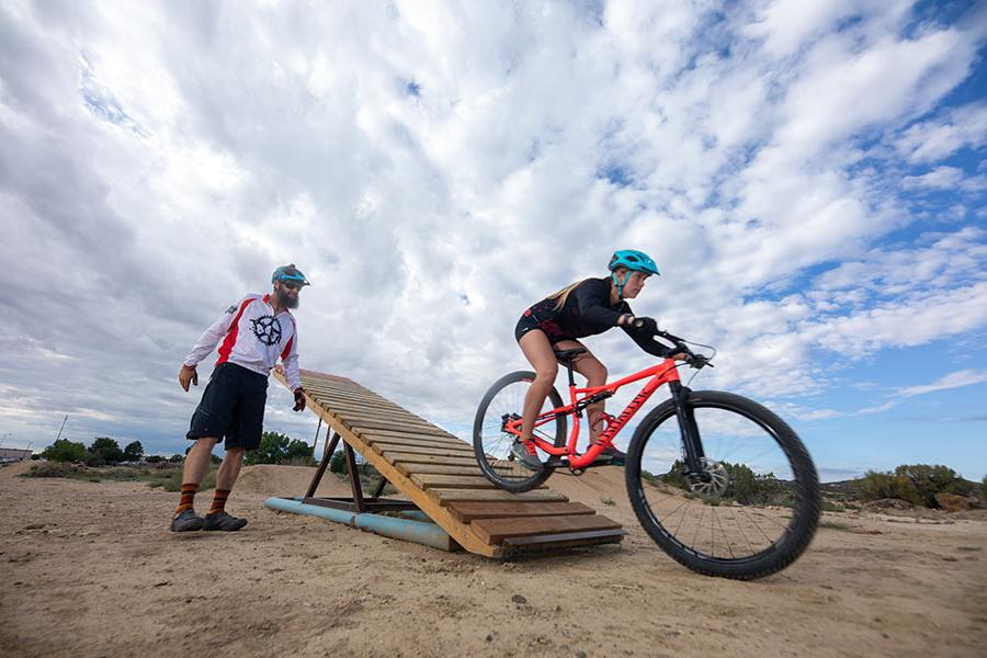 Women on her bicycle coming off a teeter ramp with a gentleman guiding her