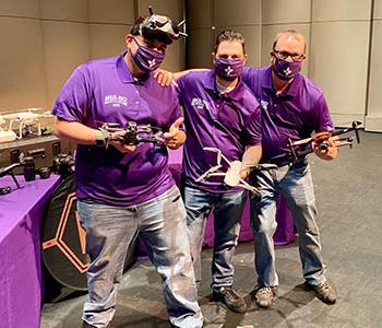 Three people holding drones.